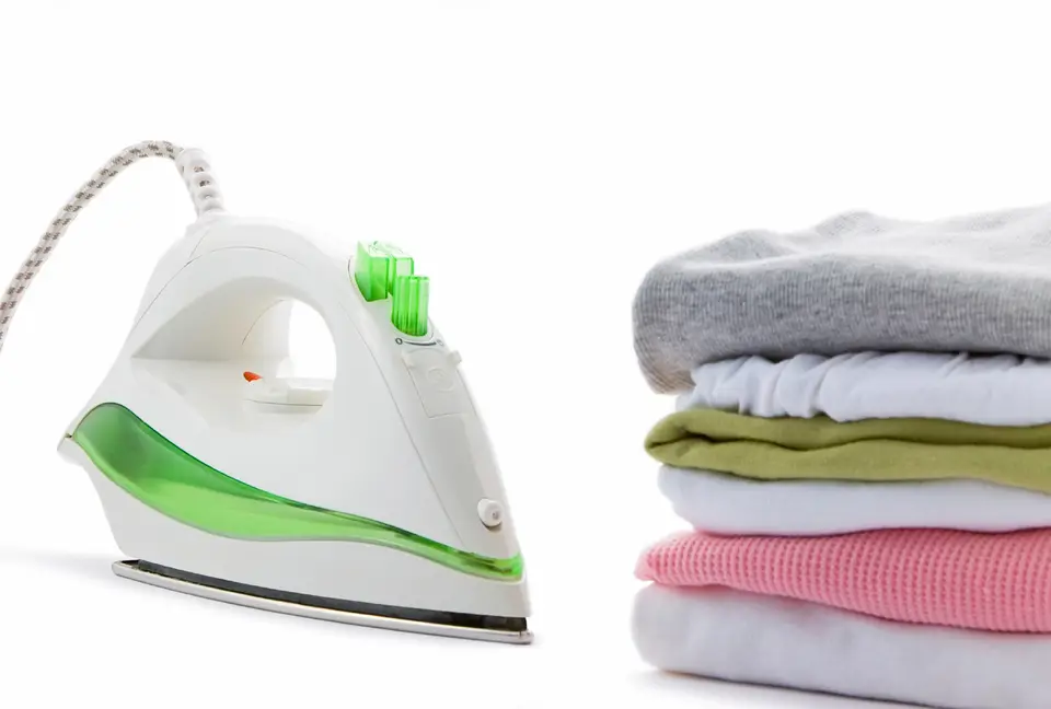 A white and green steam iron beside a stack of folded clothes