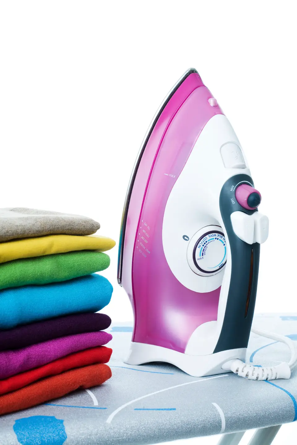 A pink steam iron on an ironing board beside a stack of folded, brightly coloured jumpers
